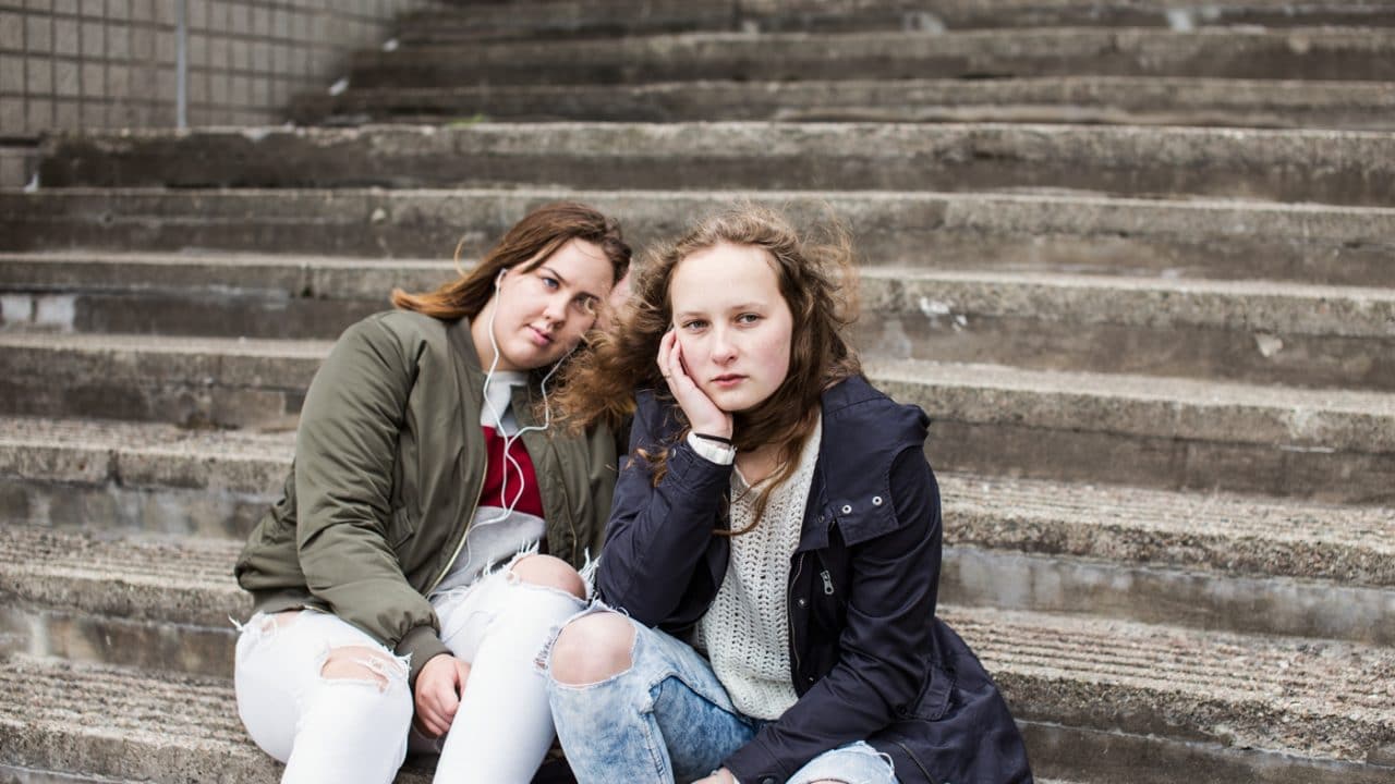 Kaksi nuorta tyttöä istuu betonirappusilla mietteliään näköisinä.