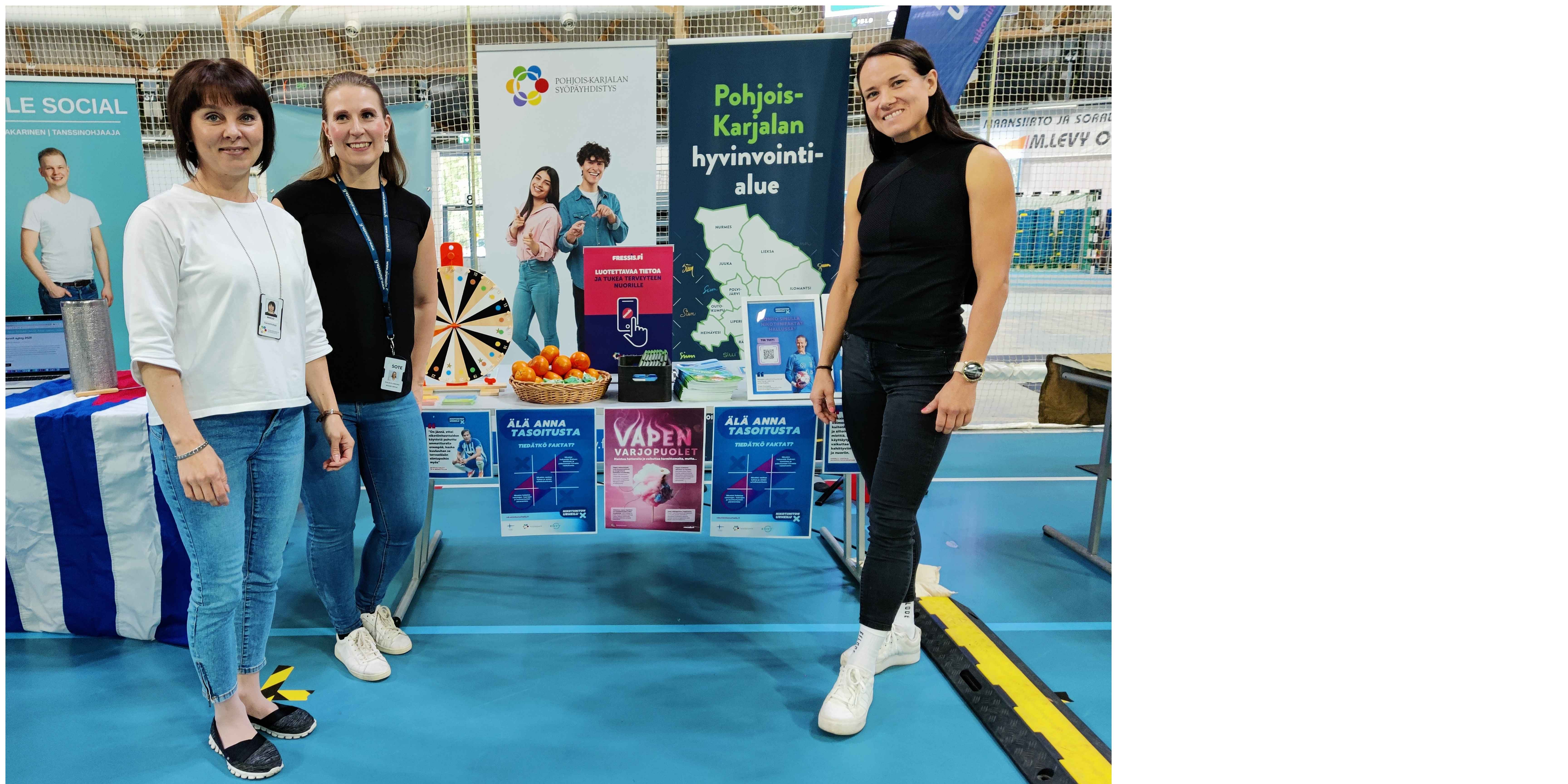 Kolme henkilöä seisoo urheilutapahtuman ständin edustalla